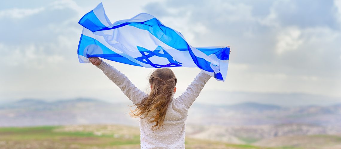 Little patriot jewish girl standing  and enjoying with the flag of Israel on blue sky background.Memorial day-Yom Hazikaron, Patriotic holiday Independence day Israel - Yom Ha'atzmaut concept